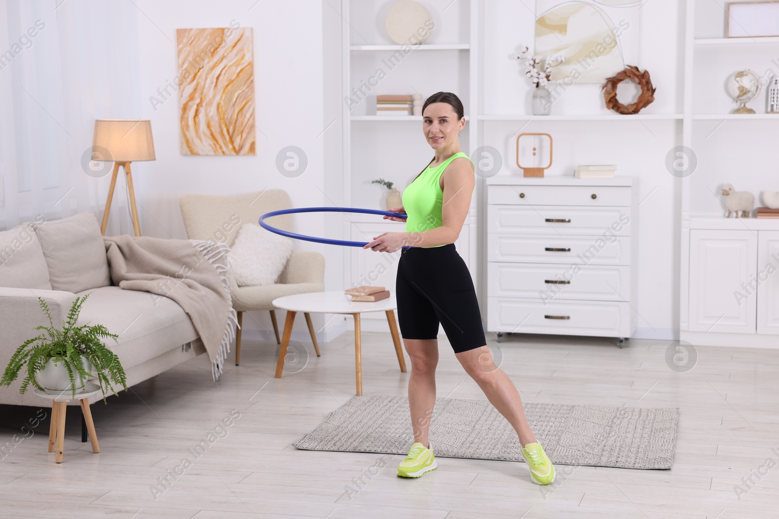 Photo of Smiling woman training with hula hoop at home