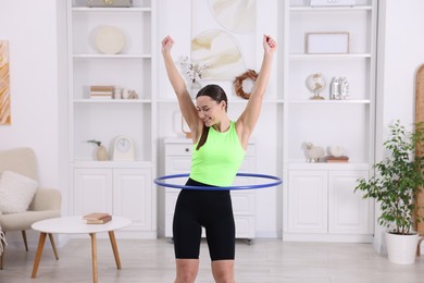 Photo of Smiling woman training with hula hoop at home