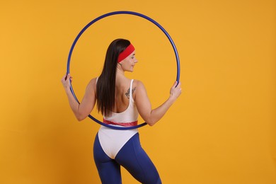 Photo of Smiling woman with hula hoop on orange background, back view