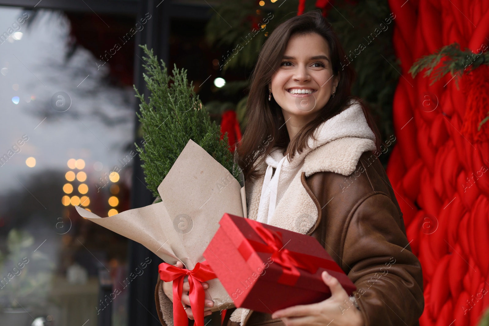 Photo of Happy woman with thuja tree and gift outdoors