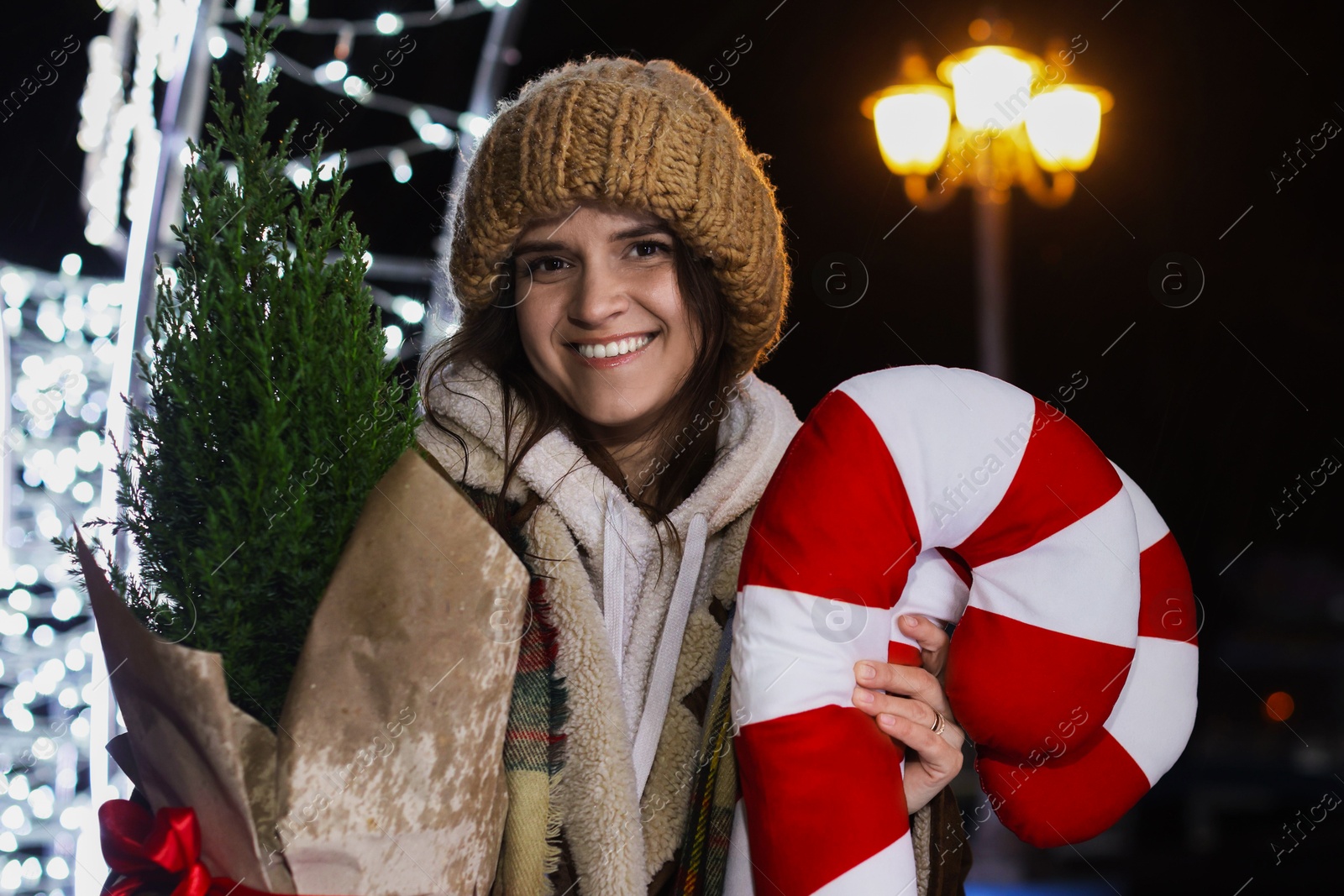 Photo of Happy woman with Christmas decor and thuja tree at night outdoors