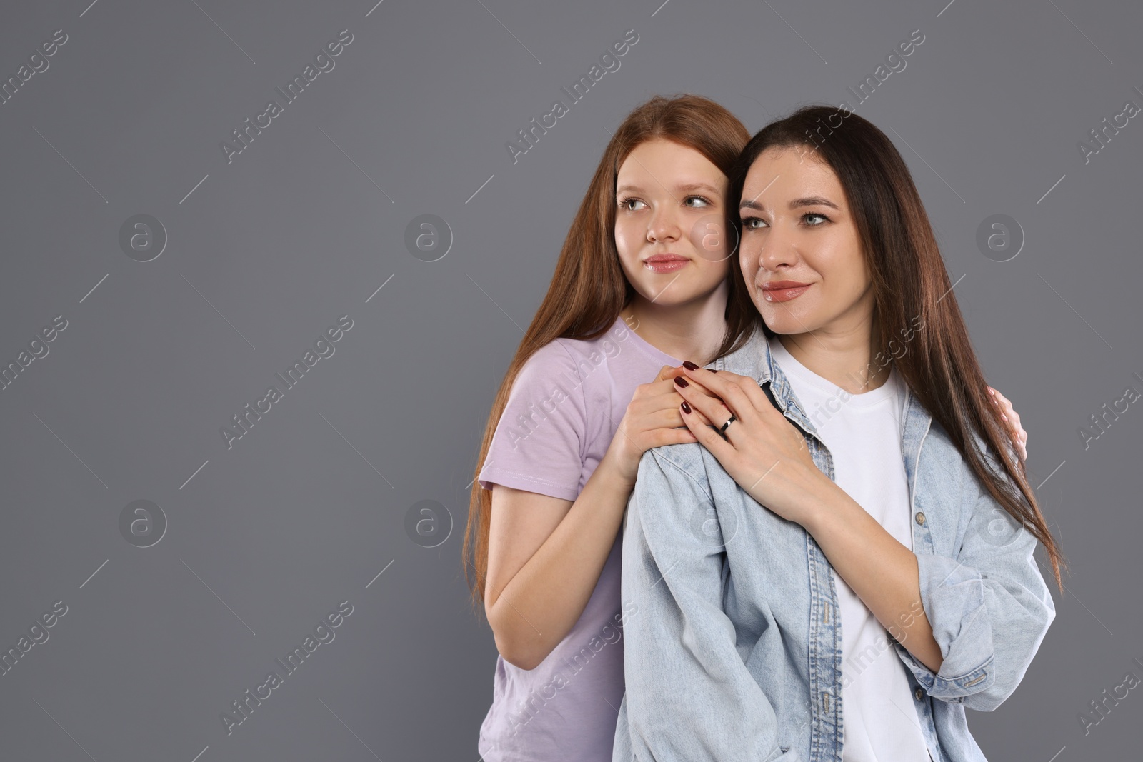 Photo of Family portrait of beautiful mother with teenage daughter on grey background, space for text