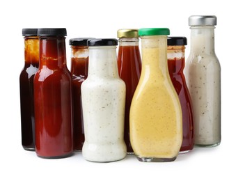 Photo of Different delicious sauces in glass bottles isolated on white