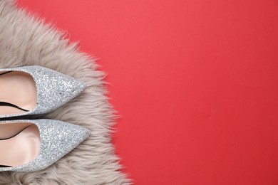 Photo of Beautiful shoes and faux fur on red background, top view. Space for text