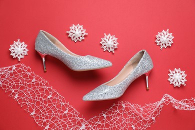 Photo of Beautiful high heeled shoes, decorative snowflakes and lace ribbon on red background, flat lay