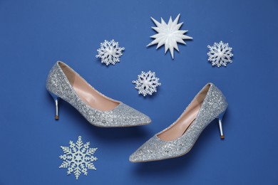 Photo of Beautiful high heeled shoes and decorative snowflakes on blue background, flat lay