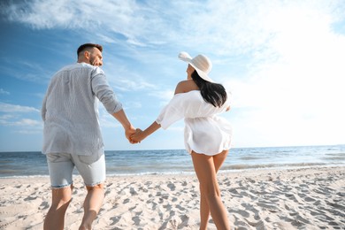 Photo of Happy couple running together on beach, back view