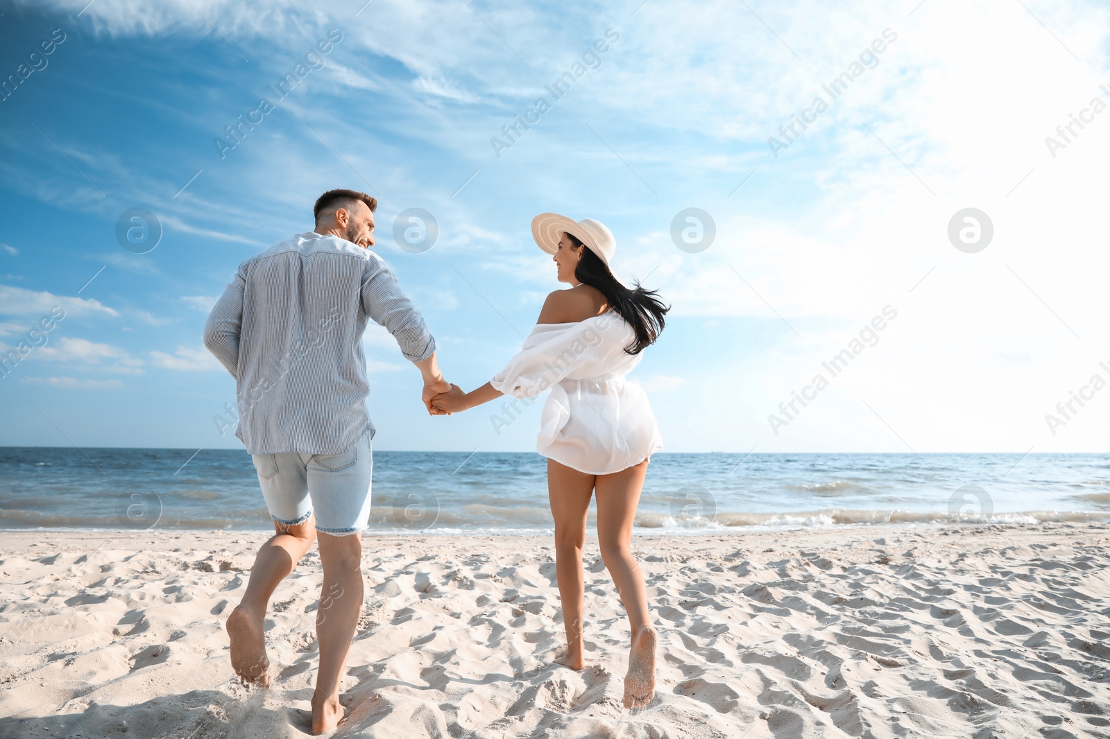 Photo of Happy couple running together on beach, back view