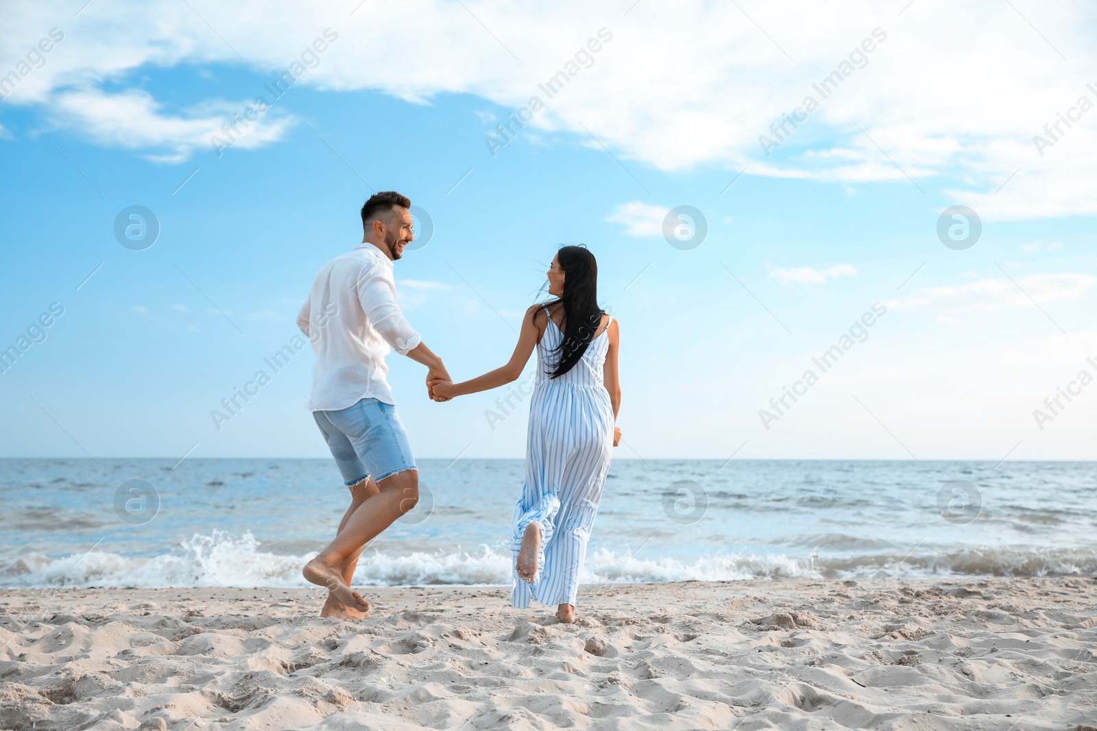 Photo of Happy couple running together on beach, back view