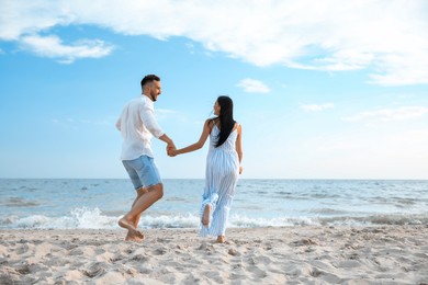 Photo of Happy couple running together on beach, back view