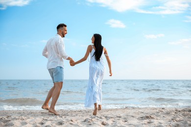 Photo of Happy couple running together on beach, back view