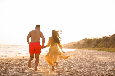 Photo of Lovely couple running together on beach at sunset, back view