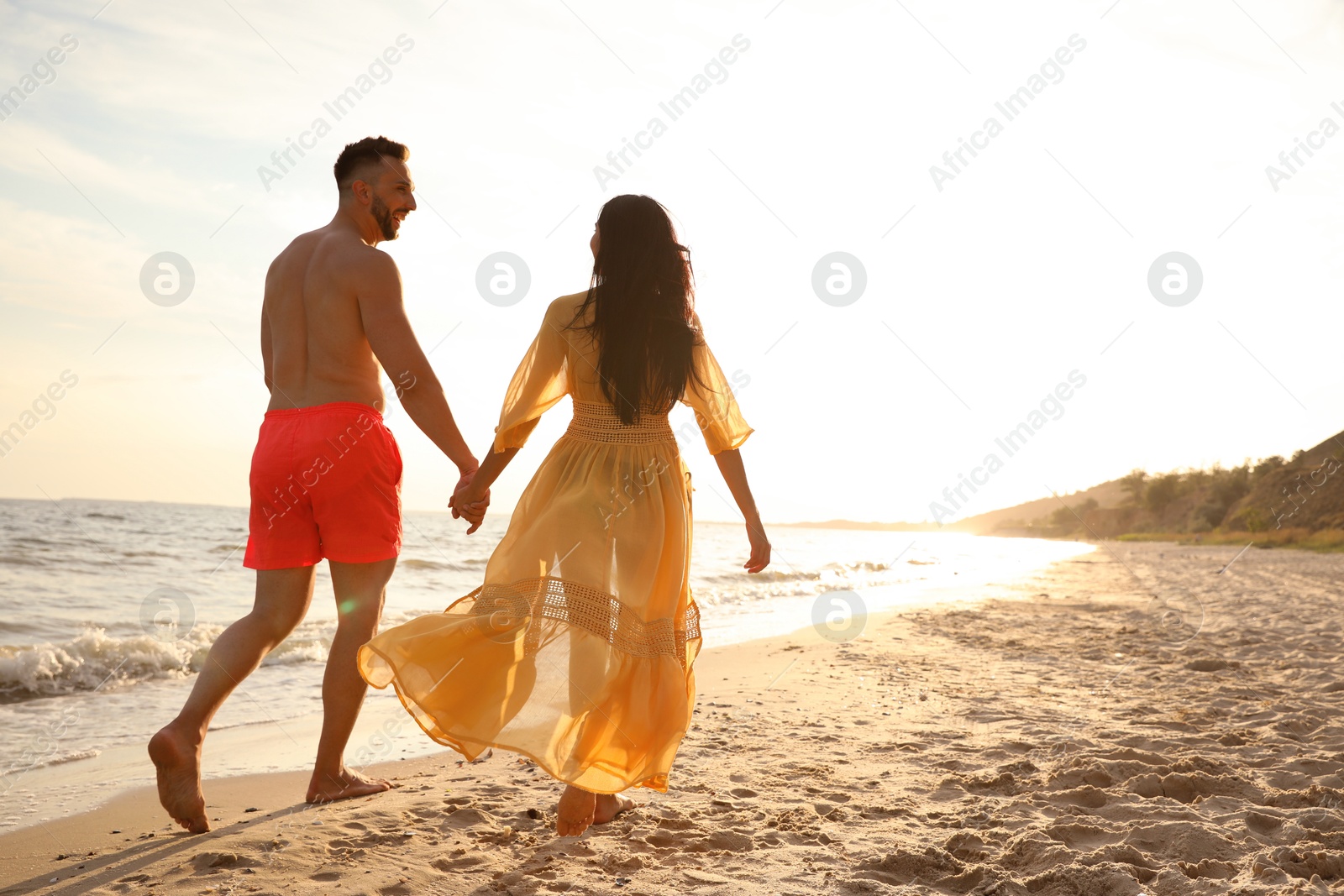 Photo of Happy couple walking together on beach at sunset, back view