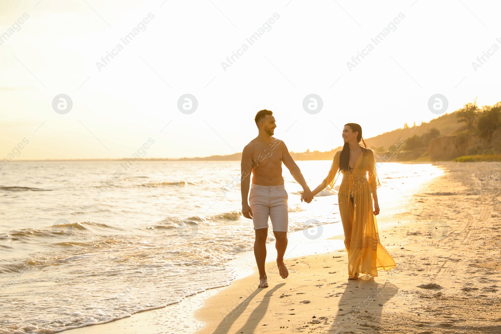 Photo of Happy young couple walking together on beach at sunset