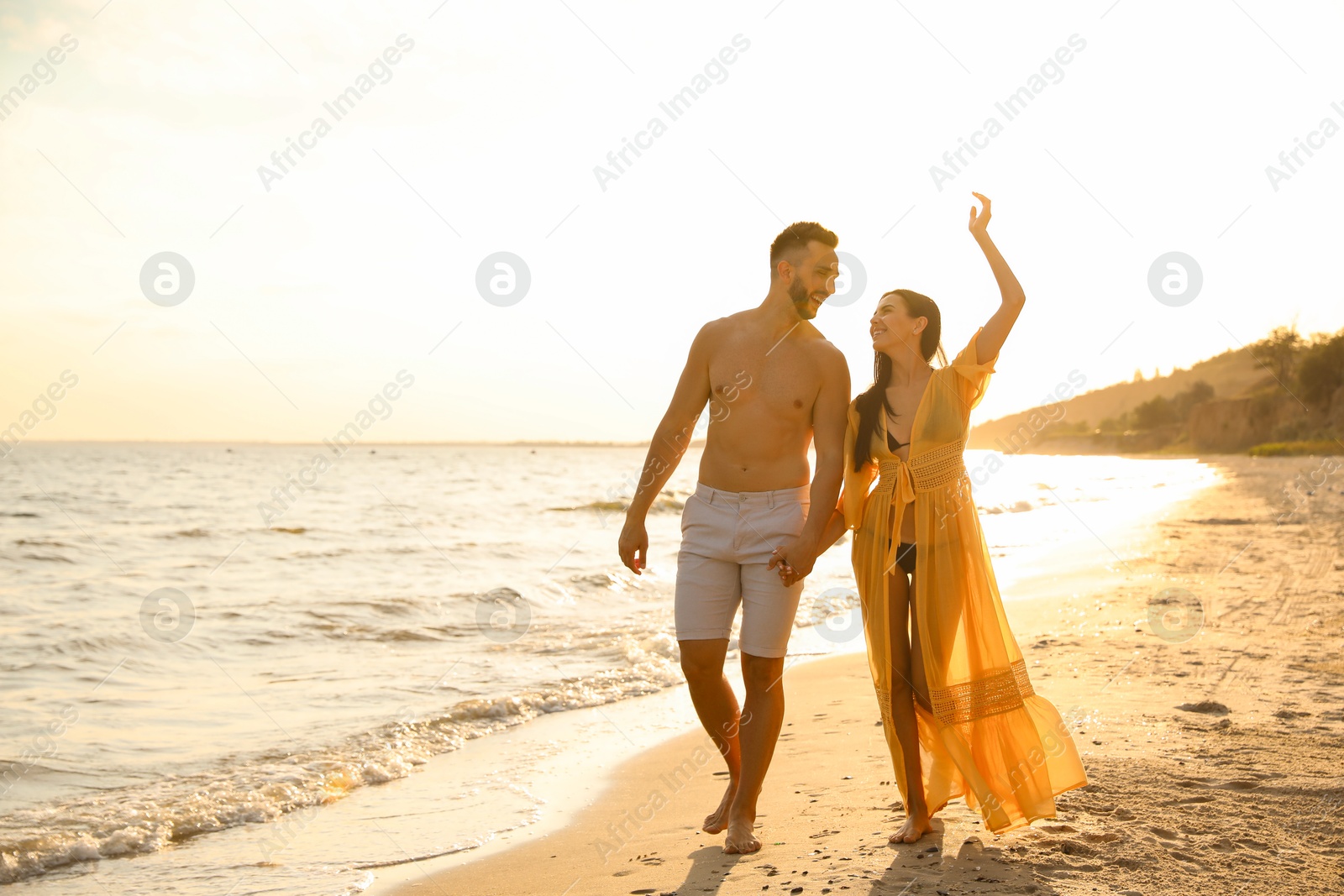 Photo of Happy young couple walking together on beach at sunset