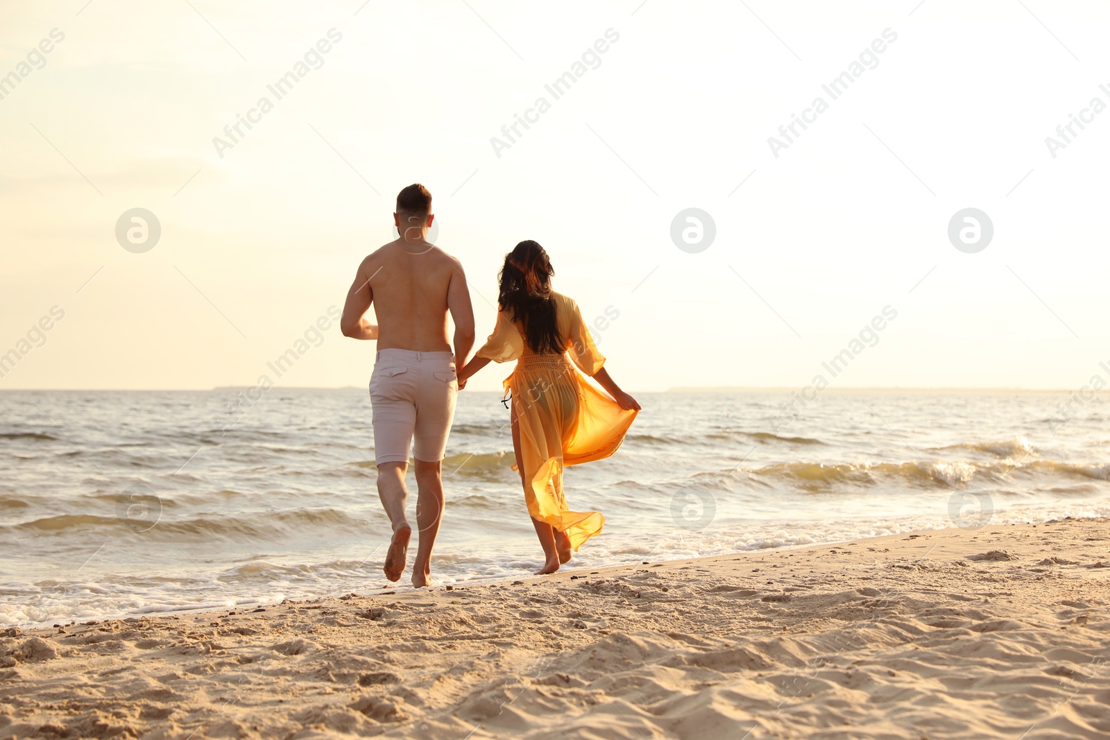 Photo of Lovely couple running together on beach at sunset, back view