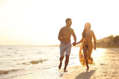 Photo of Happy young couple running together on beach at sunset