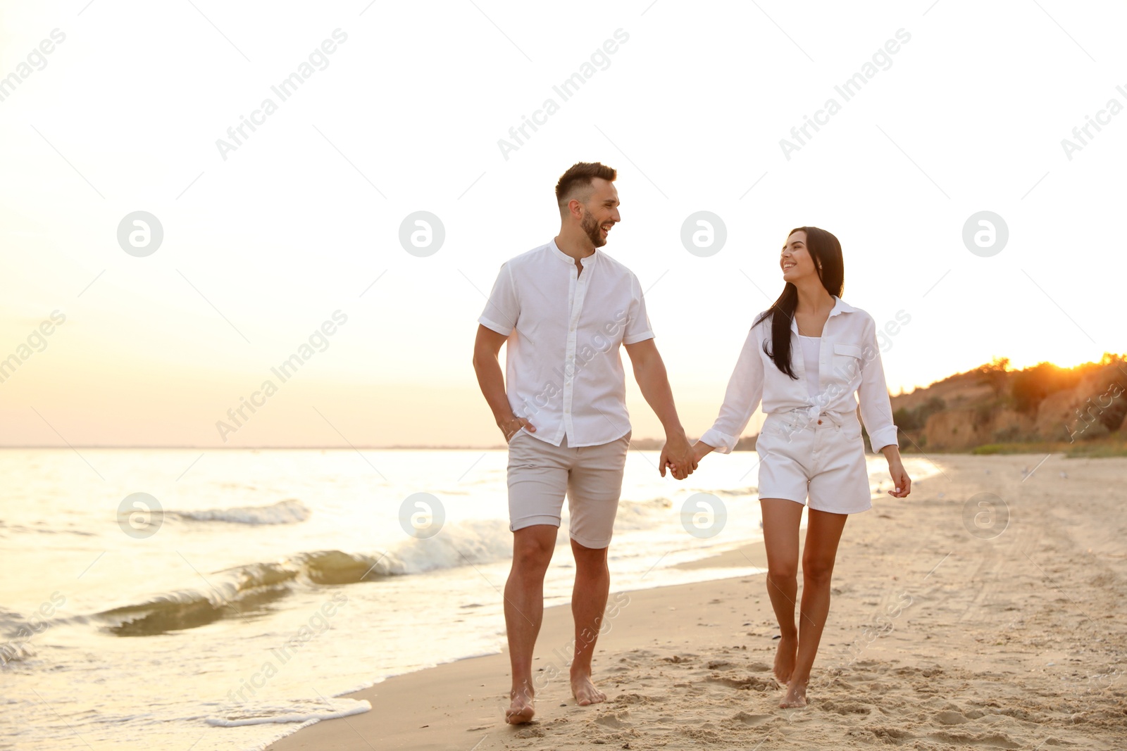 Photo of Happy young couple walking together on beach at sunset