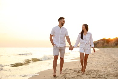 Photo of Happy young couple walking together on beach at sunset