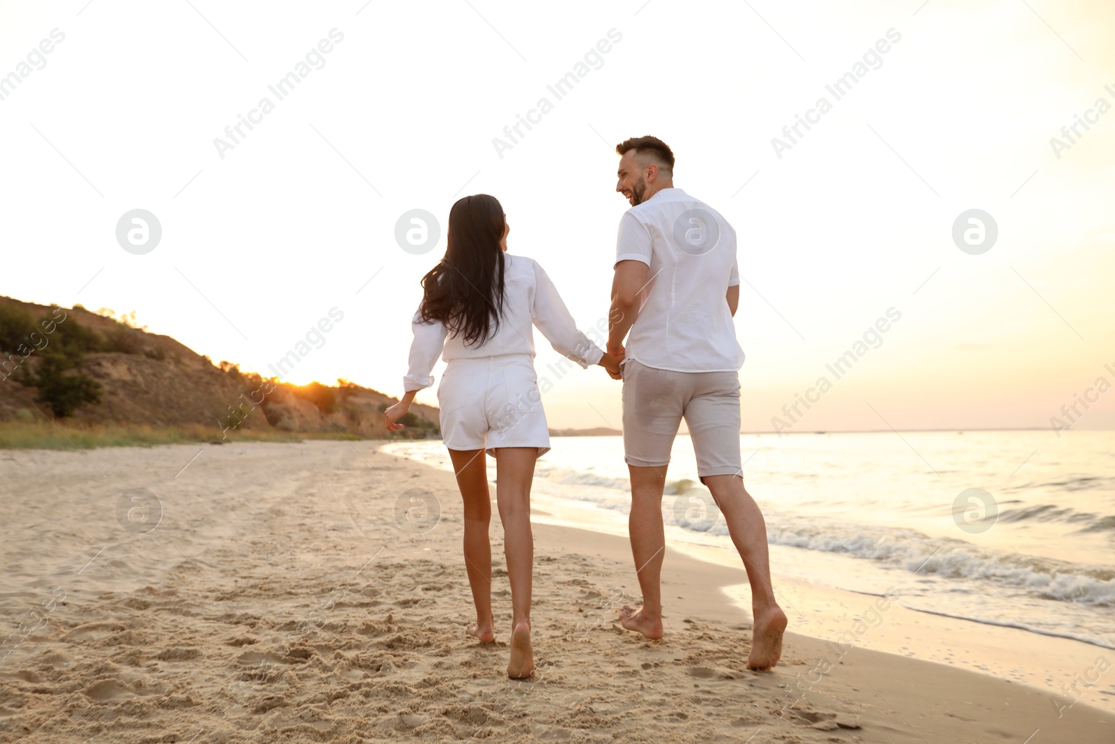 Photo of Lovely couple running together on beach at sunset, back view