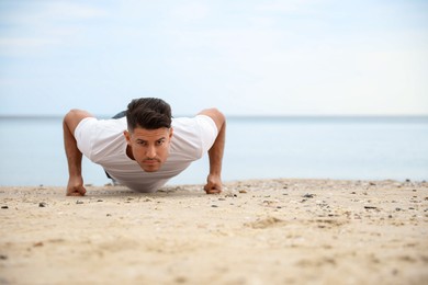 Photo of Muscular man doing push up on beach, space for text. Body training