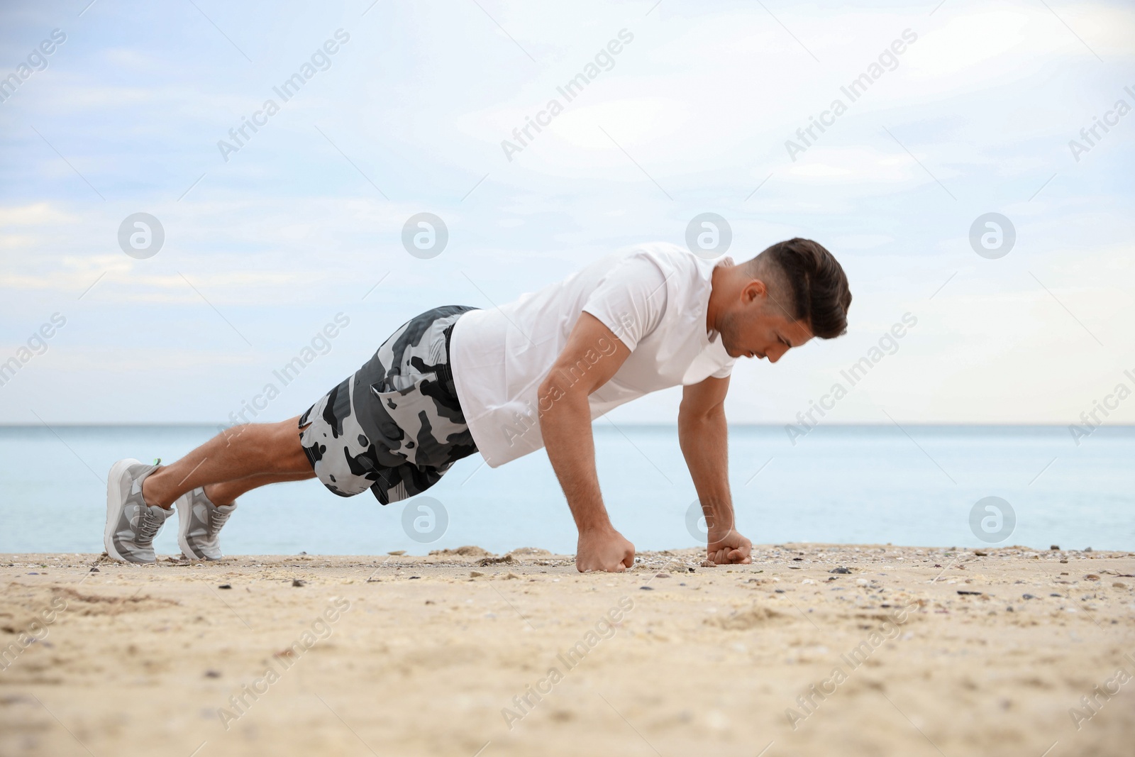 Photo of Muscular man doing push up on beach. Body training