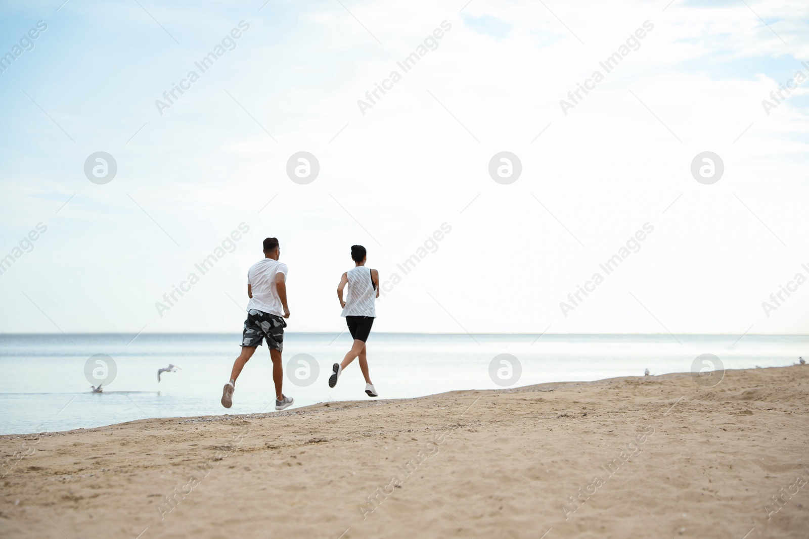 Photo of Couple running together on beach, space for text. Body training