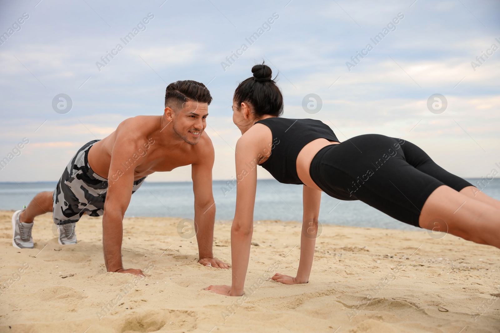 Photo of Couple doing exercise together on beach. Body training