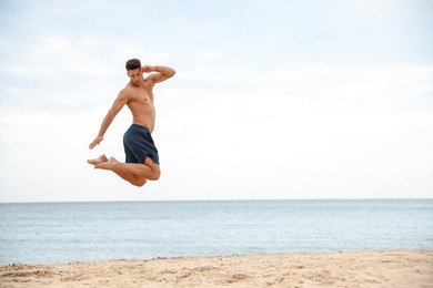 Photo of Muscular man jumping on beach, space for text. Body training