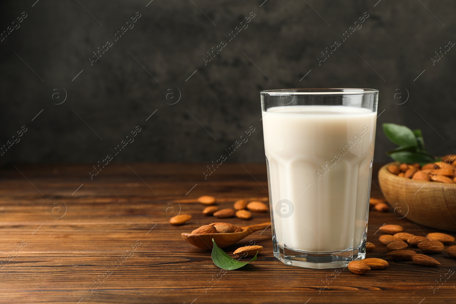 Photo of Fresh almond milk in glass and nuts on wooden table, space for text