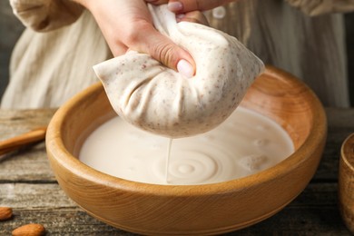 Photo of Woman making almond milk at wooden table, closeup