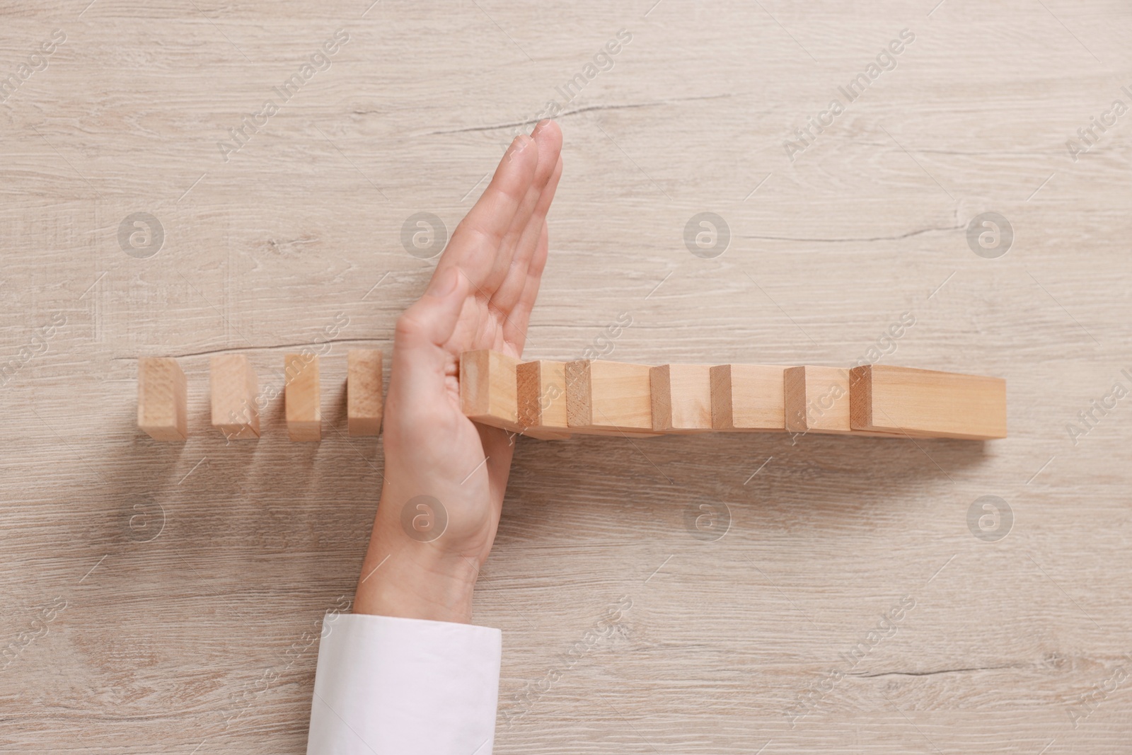 Photo of Woman stopping wooden blocks from falling at table, closeup. Domino effect