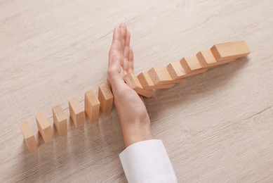 Photo of Woman stopping wooden blocks from falling at table, closeup. Domino effect