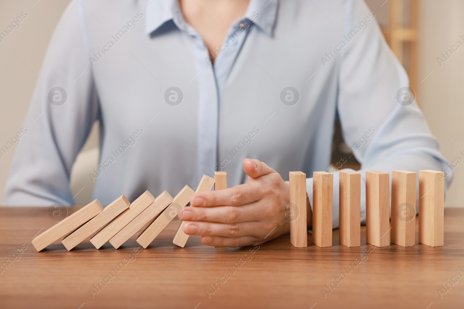 Photo of Woman stopping wooden blocks from falling at table, closeup. Domino effect