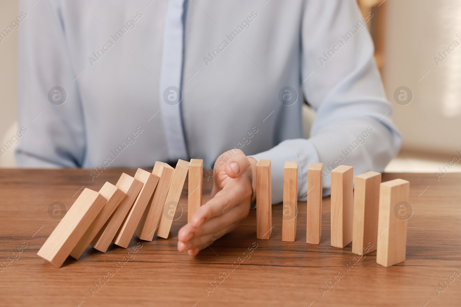 Photo of Woman stopping wooden blocks from falling at table, closeup. Domino effect