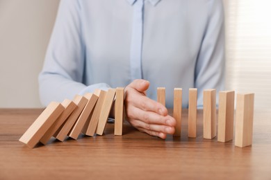 Photo of Woman stopping wooden blocks from falling at table, closeup. Domino effect