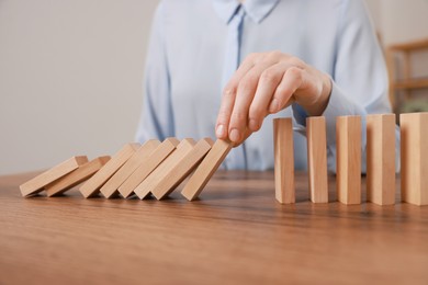 Photo of Woman stopping wooden blocks from falling at table, closeup. Domino effect