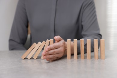 Photo of Woman stopping wooden blocks from falling at table, closeup. Domino effect