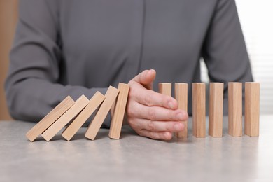 Photo of Woman stopping wooden blocks from falling at table, closeup. Domino effect