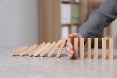 Photo of Woman stopping wooden blocks from falling at table, closeup. Domino effect