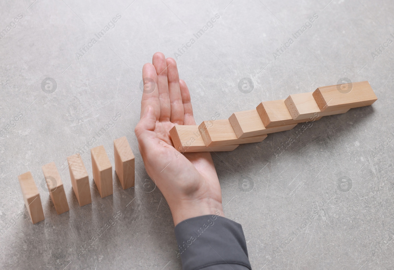 Photo of Woman stopping wooden blocks from falling on grey background, closeup. Domino effect