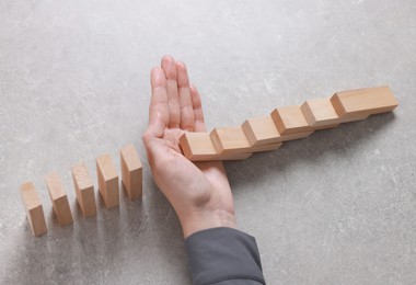 Photo of Woman stopping wooden blocks from falling on grey background, closeup. Domino effect