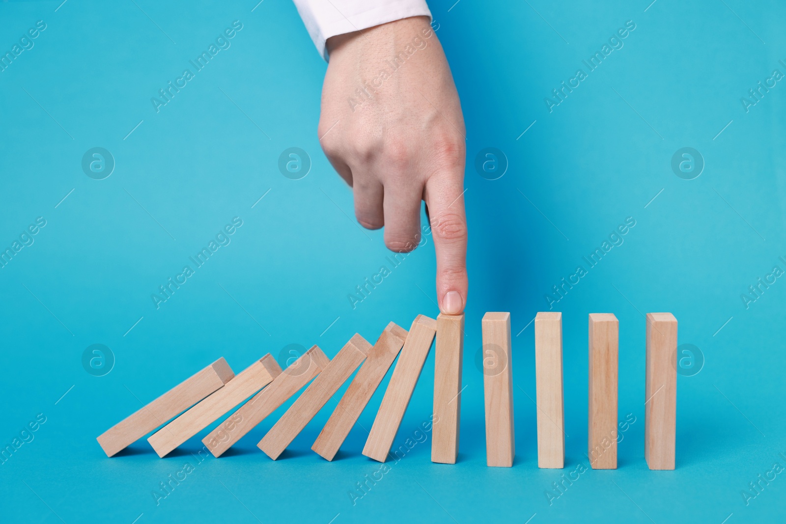 Photo of Woman stopping wooden blocks from falling on light blue background, closeup. Domino effect