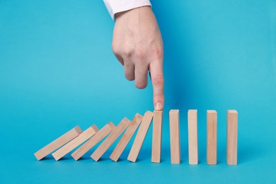 Photo of Woman stopping wooden blocks from falling on light blue background, closeup. Domino effect