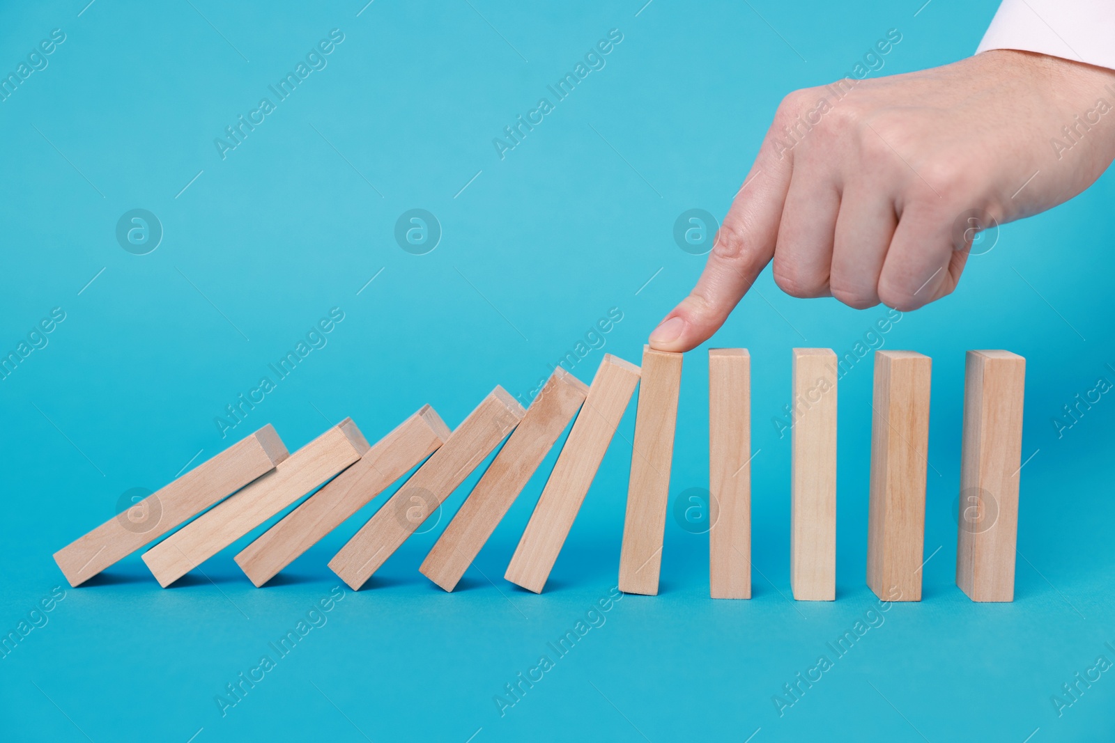 Photo of Woman stopping wooden blocks from falling on light blue background, closeup. Domino effect