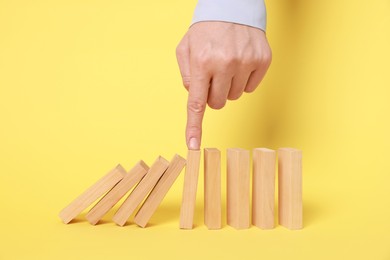 Photo of Woman stopping wooden blocks from falling on yellow background, closeup. Domino effect