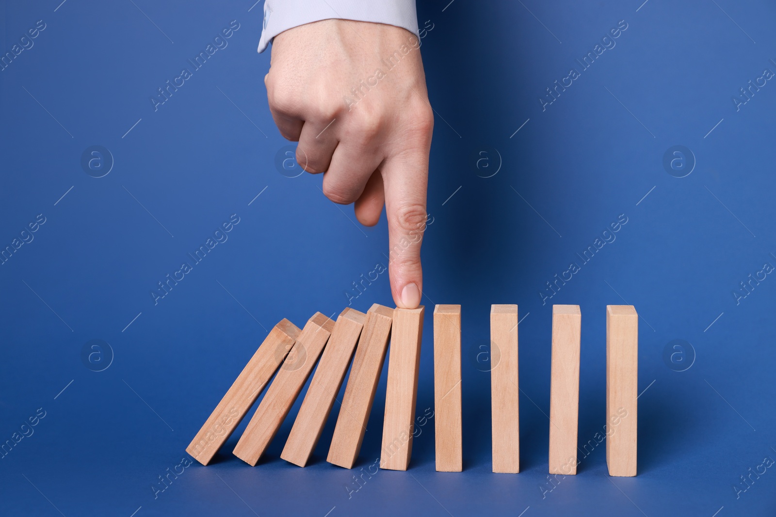 Photo of Woman stopping wooden blocks from falling on blue background, closeup. Domino effect