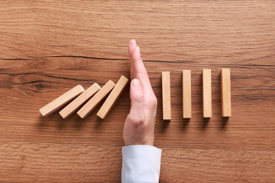 Photo of Man stopping wooden blocks from falling at table, top view. Domino effect