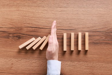 Photo of Man stopping wooden blocks from falling at table, top view. Domino effect