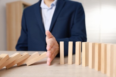 Photo of Man stopping wooden blocks from falling at table, closeup. Domino effect